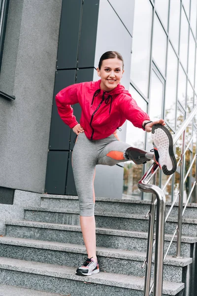 Sonriente deportista discapacitada con prótesis calentándose en la calle - foto de stock