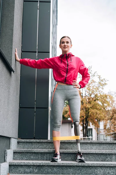 Full length view of smiling disabled sportswoman training with resistance band on street — Stock Photo