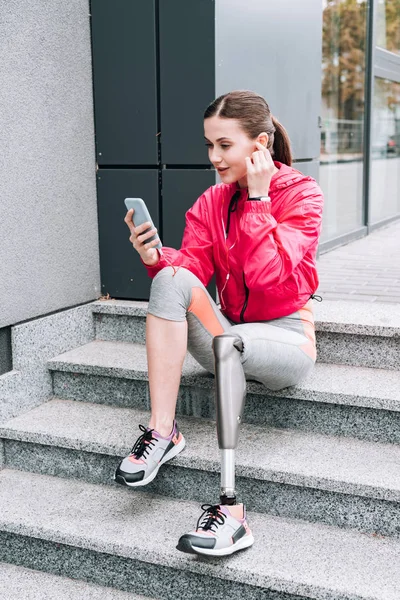 Disabled sportswoman using smartphone while sitting on stairs on street — Stock Photo