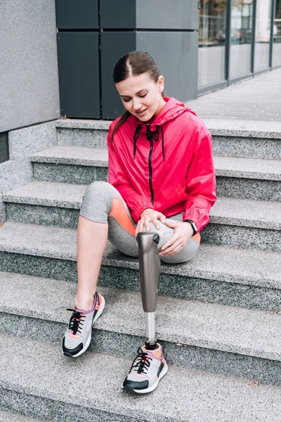 Disabled sportswoman with prosthesis sitting on stairs on street — Stock Photo