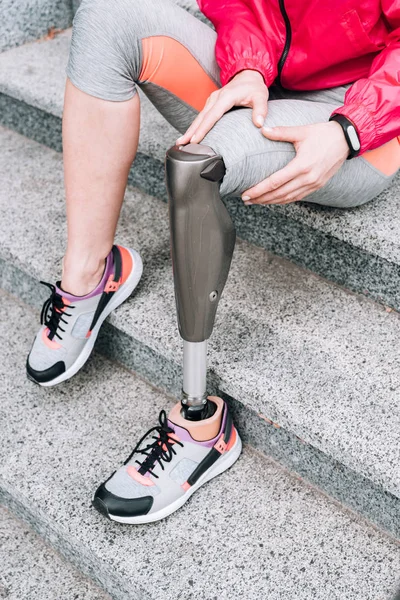 Vista parcial de la deportista discapacitada con prótesis sentada en las escaleras - foto de stock