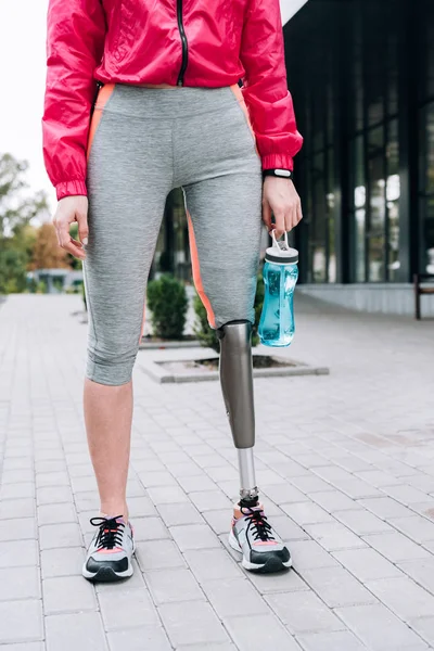 Partial view of disabled sportswoman holding sport bottle on street — Stock Photo