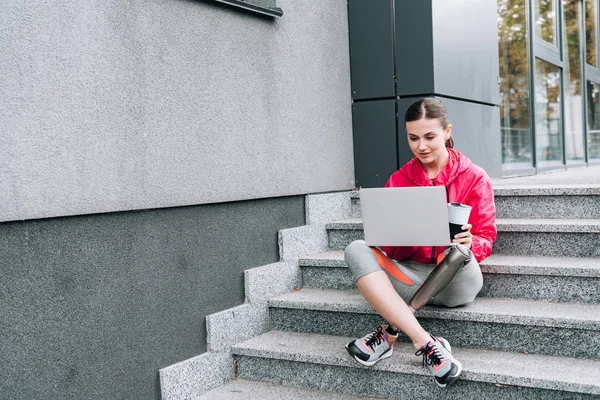 Спортсменка-инвалид с помощью ноутбука, сидя на лестнице на улице — стоковое фото