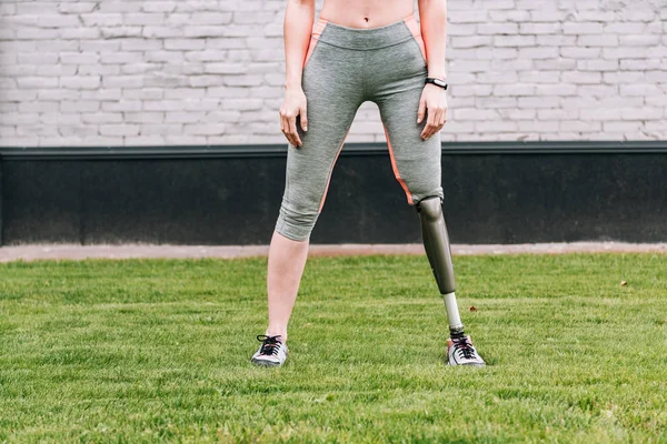 Partial view of disabled sportswoman with fitness tracker on grass — Stock Photo