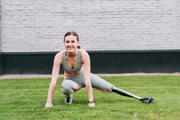 Sportiva disabile sorridente con protesi che si estende sull'erba — Foto stock