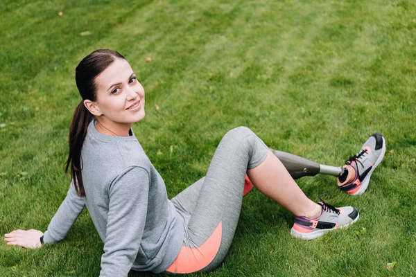 Усміхнена спортсменка з протезом сидить на траві — стокове фото