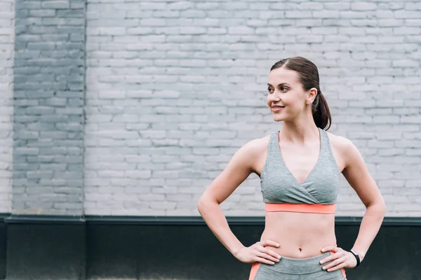 Deportista sonriente de pie con las manos en las caderas en la calle - foto de stock