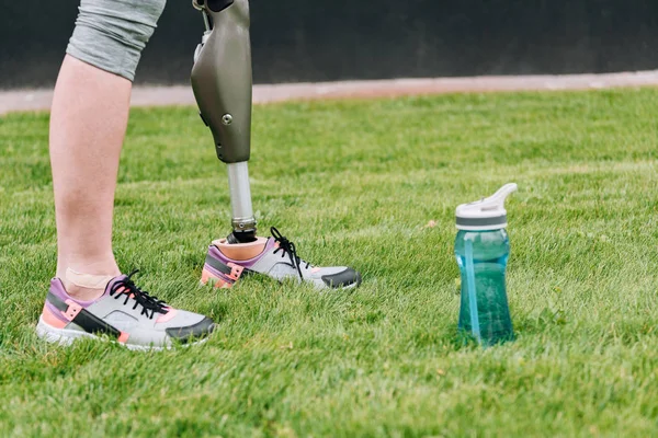 Partial view of disabled sportswoman standing near sport bottle on grass — Stock Photo