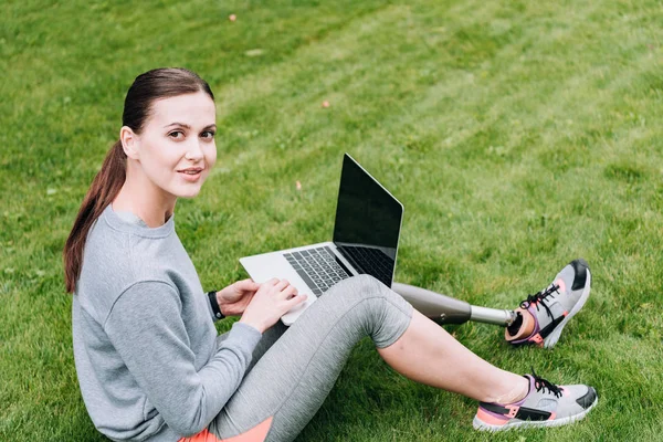 Sportif handicapé utilisant un ordinateur portable avec écran vide tout en étant assis sur l'herbe — Photo de stock