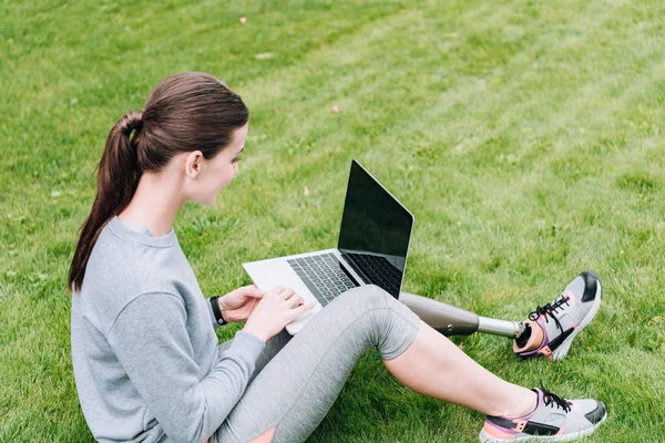 Спортсменка-инвалид с помощью ноутбука с чистым экраном, сидя на траве — Stock Photo