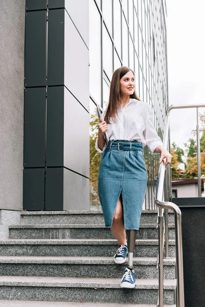 Вид в полный рост женщины-инвалида в джинсовой юбке, держащей ноутбук на улице — стоковое фото
