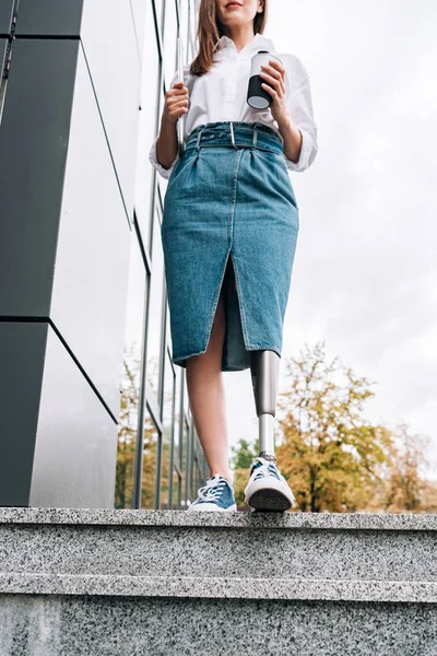 Partial view of disabled woman in denim skirt holding laptop and cup on street — Stock Photo