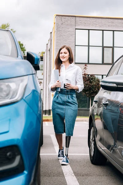 Full length view of smiling disabled woman with laptop near cars on street — Stock Photo