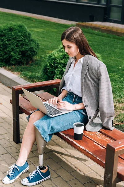Инвалид женщина сидит на скамейке и с помощью ноутбука на улице — стоковое фото
