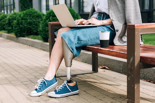 Ausgeschnittene Ansicht einer behinderten Frau, die auf einer Bank sitzt und Laptop auf der Straße benutzt — Stockfoto