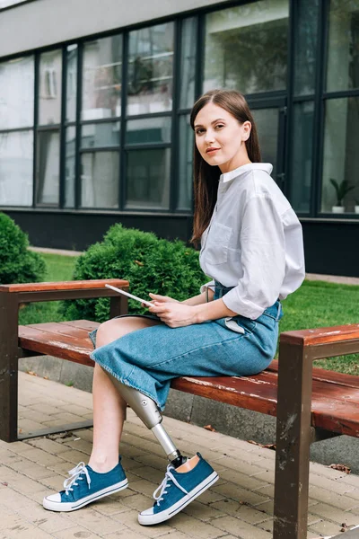 Atractiva mujer discapacitada sentada en el banco con tableta digital - foto de stock