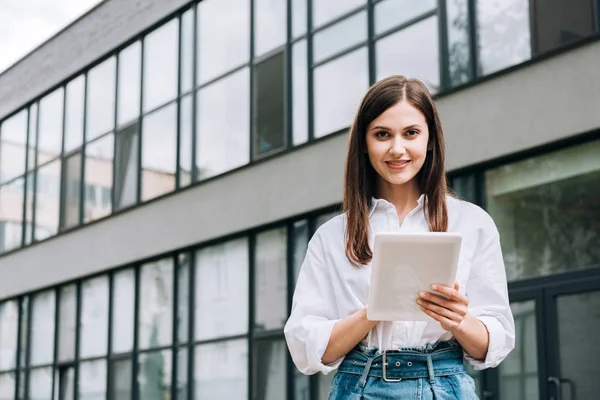 Lächelnde junge Frau im weißen Hemd mit digitalem Tablet auf der Straße — Stockfoto