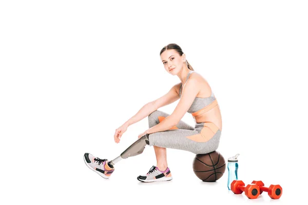 Lächelnde Behindertensportlerin mit Prothese sitzt auf Basketballball auf Weiß — Stockfoto