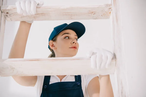 Hübsche junge Malerin in Uniform klettert auf Leiter und schaut weg — Stockfoto