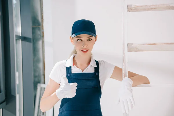 Pretty young painter in uniform showing thumb up while looking at camera — Stock Photo