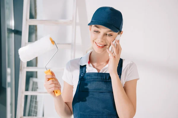 Hübsche junge Malerin spricht mit Smartphone und hält Farbwalze in der Hand — Stockfoto