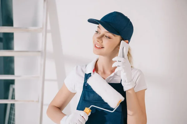 Atraente jovem pintor segurando rolo de pintura e falando no smartphone — Fotografia de Stock