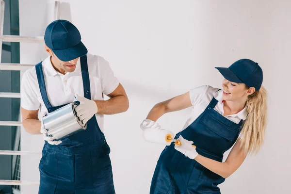 Pintores alegres divertirse mientras sostiene lata con pintura y rodillo de pintura - foto de stock