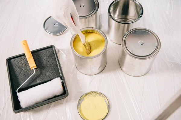 Vue recadrée de l'homme plongeant le pinceau dans la boîte avec de la peinture jaune — Photo de stock