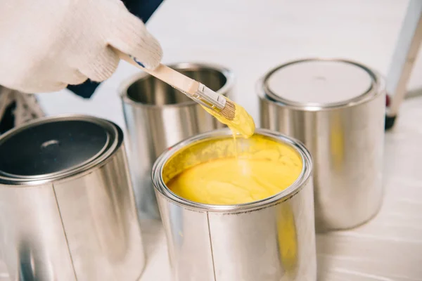 Cropped view of man holding paintbrush near paint with yellow can — Stock Photo