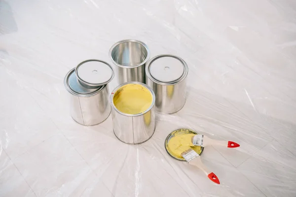 Latas com tinta e pincéis amarelos no piso branco coberto com celofane — Fotografia de Stock