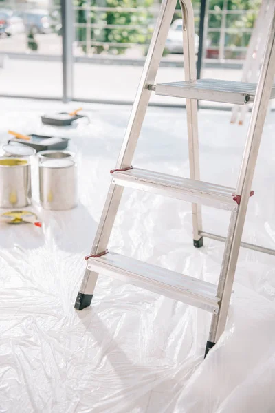 Foco seletivo de escada na sala com latas de tinta no piso branco coberto com celofane — Fotografia de Stock