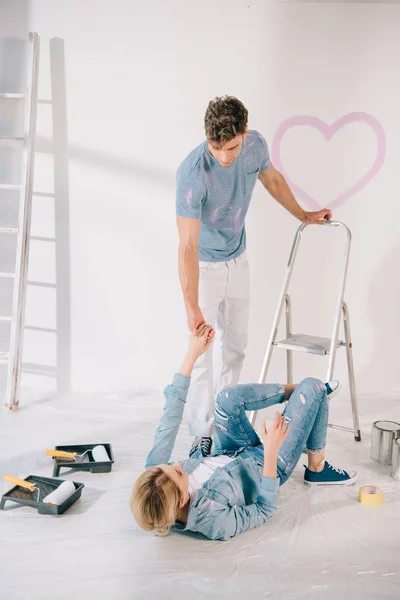 Joven ayudando novia caído de escalera y acostado en el suelo - foto de stock