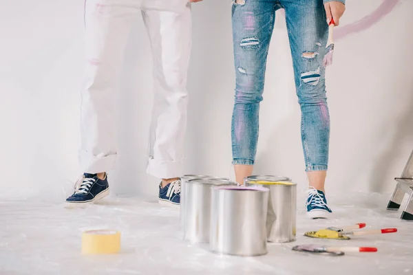 Vista recortada del hombre y la mujer de pie junto a la pared blanca cerca de latas con pintura - foto de stock