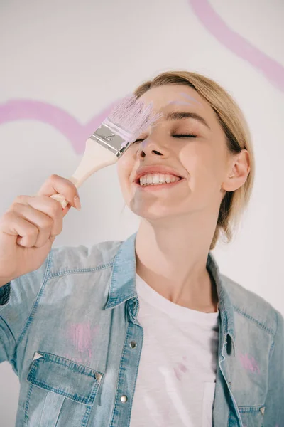 Happy young woman standing with closed eyes and holding pink paintbrush — Stock Photo