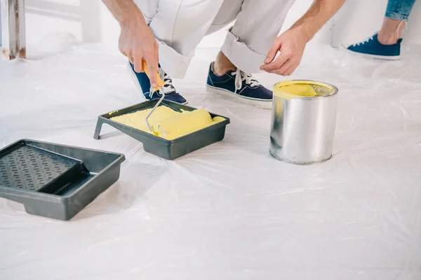 Cropped view of man putting paint roller into yellow paint — Stock Photo