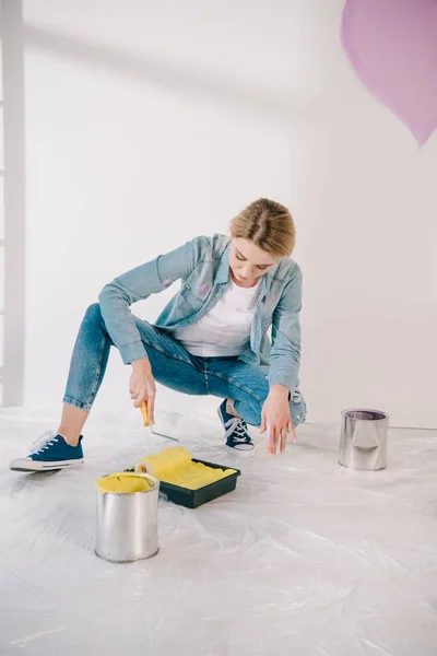 Attrayant jeune femme mettant rouleau de peinture dans le plateau de rouleau avec de la peinture jaune — Photo de stock