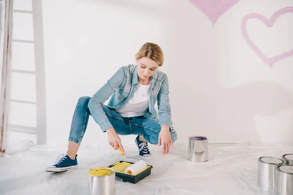 Bella giovane donna mettendo rullo di vernice in vassoio rullo con vernice gialla — Foto stock