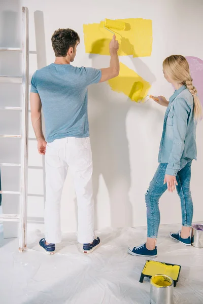 Pareja joven pintando pared blanca con rodillos de pintura en casa - foto de stock