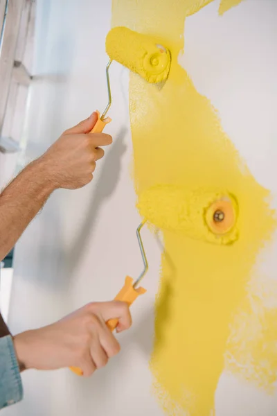 Vista parcial de la pared de pintura de hombre y mujer en amarillo con rodillos de pintura - foto de stock