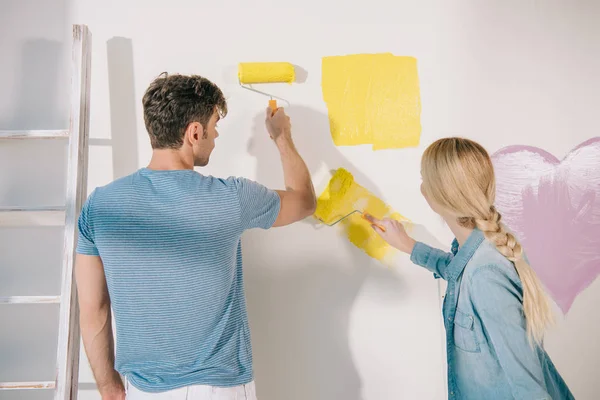 Jovem casal pintura parede branca em amarelo com rolos de pintura — Fotografia de Stock