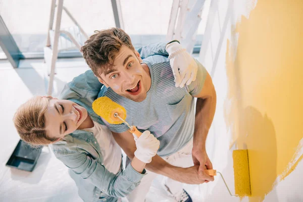 Cheerful girl having fun while frightening boyfriend with paint roller — Stock Photo