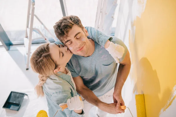 Alto ângulo vista de menina beijando namorado pintura parede em amarelo — Fotografia de Stock