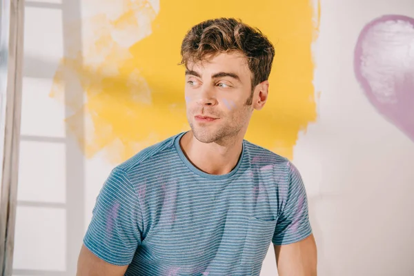 Schöner junger Mann, der in der Nähe weißer, gelb lackierter Wände wegschaut — Stockfoto