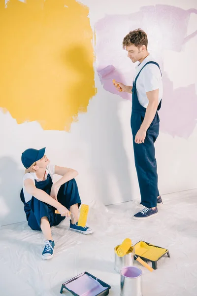 Guapo joven pintor mirando atractivo colega sentado en el suelo - foto de stock