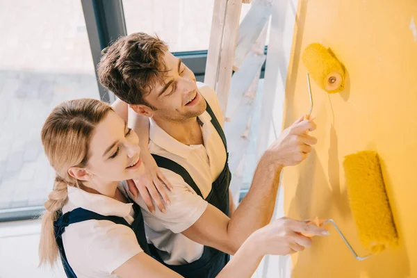 Vue grand angle de jeunes peintres en salopette peinture murale en jaune — Photo de stock