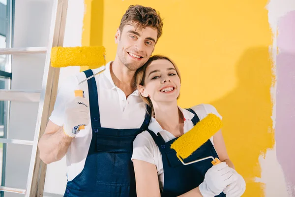 Two cheerful painters smiling at camera while holding paint rollers — Stock Photo