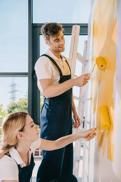 Dos jóvenes pintores pintando la pared en amarillo con rodillos de pintura - foto de stock