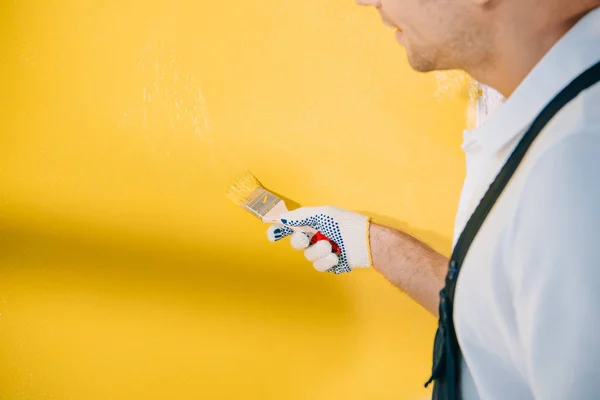 Vista recortada de la pared de pintura joven pintor en color amarillo con pincel - foto de stock