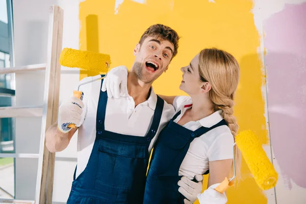 Cheerful painter looking at camera while standing near attractive colleague — Stock Photo