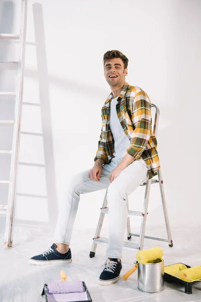 Joven guapo sonriendo sentado en la escalera y mirando a la cámara — Stock Photo